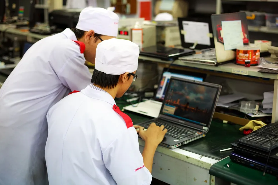 Two technicians in uniforms working on laptops in a laboratory setting. Focus on teamwork and technology.
