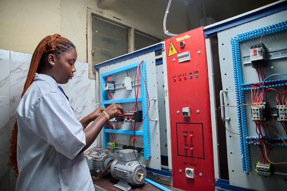 Young female technician repairing electrical control panel in industrial setting.