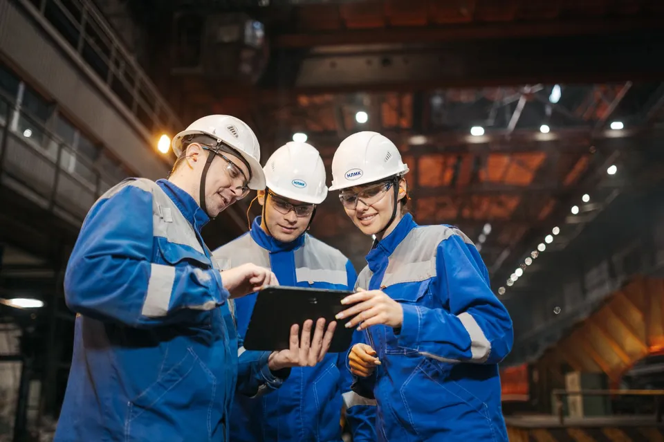 Group of engineers discussing project on a tablet in a factory setting.