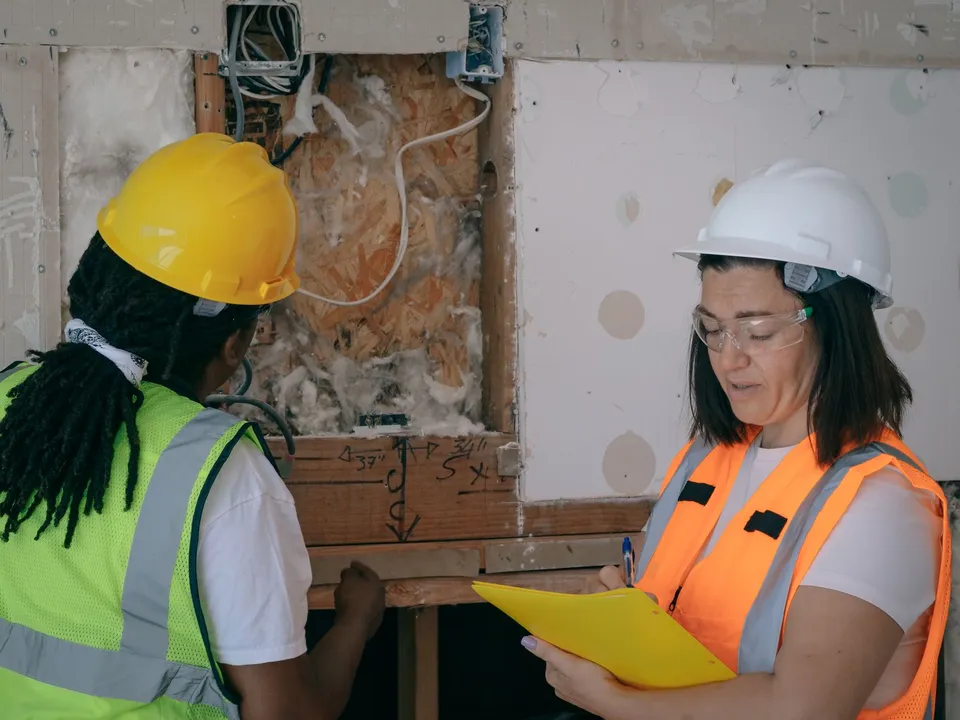 Two workers in protective gear inspecting and taking notes during a construction site electrical inspection.