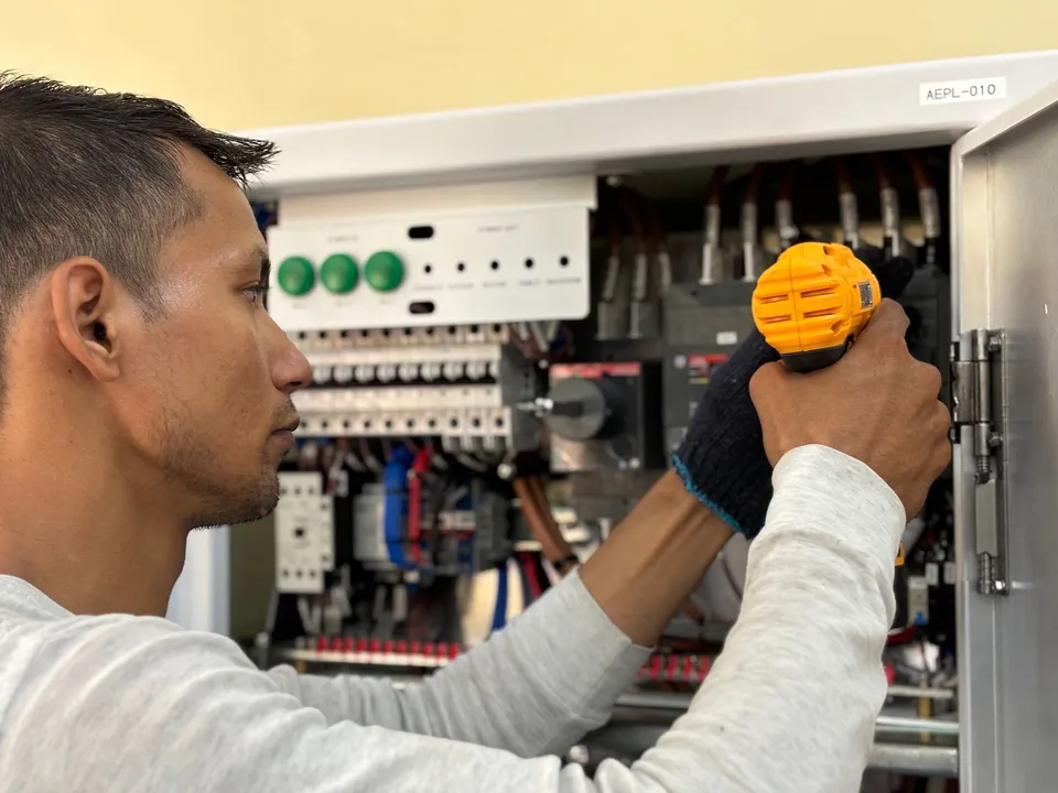 Skilled electrician using a drill to repair electrical equipment indoors. Focus on precision and safety.
